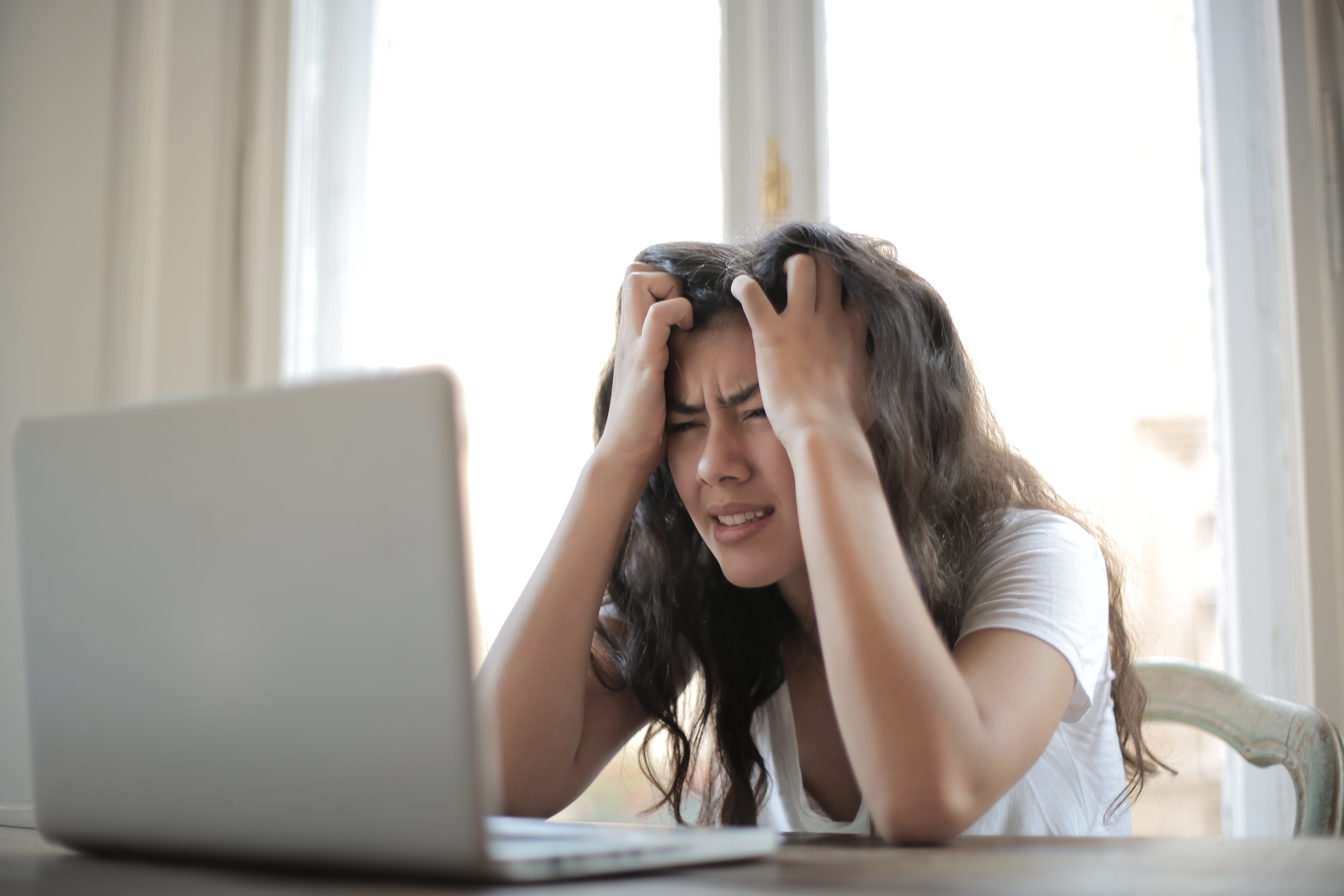 Een vrouw achter een laptop met de handen in het haar van frustratie. Foto van Pexels door Andrea Piacquadio